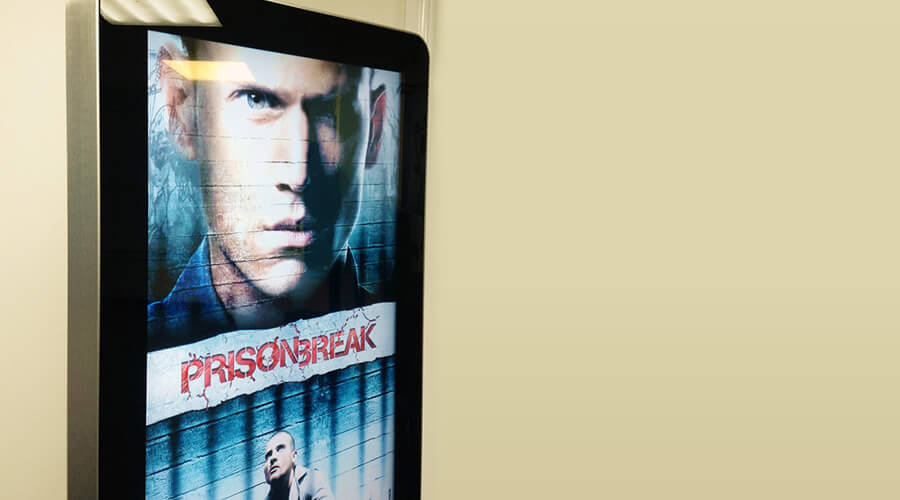 Portrait digital poster display in a cinema lobby showing film and TV promotional artwork.
