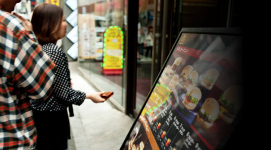 Customer browsing a digital menu display showing burger options at a fast-food restaurant window.