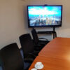 55 inch interactive touch display wall-mounted in a small meeting room, showing on-screen menu icons over a city skyline image, with conference table and chairs.