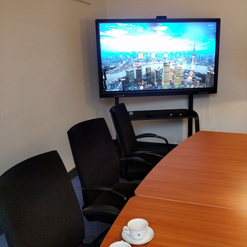 55" Interactive Touch Display with MeetingPad Software – Meeting Room Installation 55 inch interactive touch display wall-mounted in a small meeting room, showing on-screen menu icons over a city skyline image, with conference table and chairs.