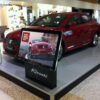 22 inch digital display mounted on a plinth beside a car showroom exhibit, showing vehicle advertising.