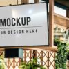 Mock-up digital signage screen mounted above a bar-style shelving display, showing placeholder "MOCKUP – Your design here" text among bottles and greenery.