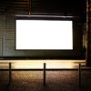 Blank illuminated digital signage screen mounted outdoors at night in a quiet, empty pedestrian area, showing no active content.