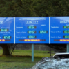 Large outdoor LED KPI display board mounted on posts at an industrial site, showing live safety, quality, and delivery performance figures across three panels.