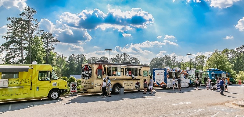 Row of food trucks with printed vinyl signage lined up in an outdoor car park, with customers queuing at the stalls.