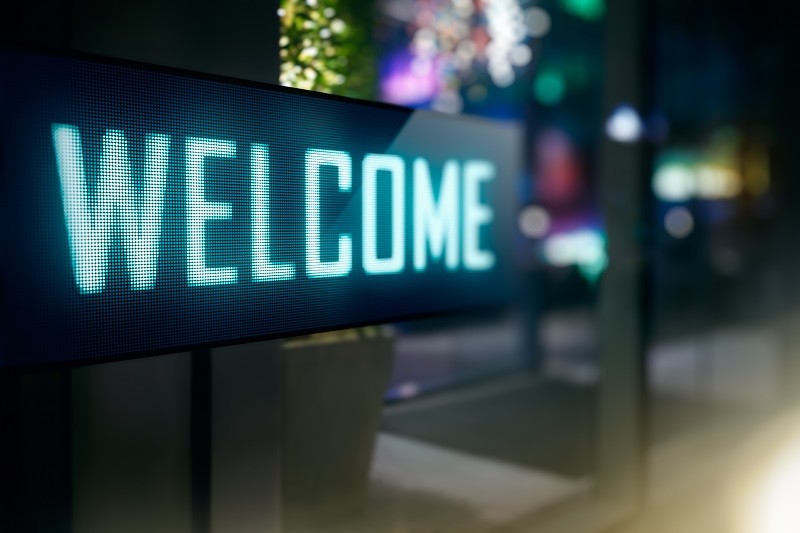 Illuminated LED sign displaying "WELCOME" at a hotel entrance at night, with ambient lighting visible in the background.