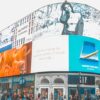 Large curved outdoor LED billboard wrapping around a corner building, displaying multiple rotating brand advertisements above a busy pedestrian street.