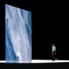 Rendered concept of a tall, thin vertical LED display column resembling a ribbon of fabric, part of a large-scale art installation viewed by visitors below.