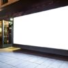 Blank illuminated shopfront window display mock-up at night, showing an empty white screen ready for advertising content within a large storefront window frame.