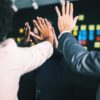 Colleagues raising hands together in a group high-five in front of a wall covered in colourful sticky notes, reflecting team collaboration and shared communication.