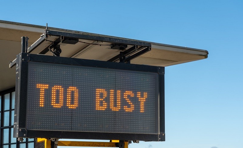 Portable outdoor LED sign displaying "TOO BUSY" against a clear blue sky, mounted on a trailer unit with a solar panel.