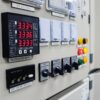Digital multifunction panel meter mounted on an industrial electrical control panel, displaying live voltage readings.