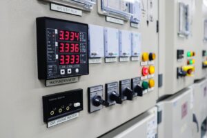Digital multifunction panel meter mounted on an industrial electrical control panel, displaying live voltage readings.