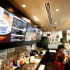 Digital menu board screens displayed above the counter of a coffee shop, showing drinks and promotional imagery.