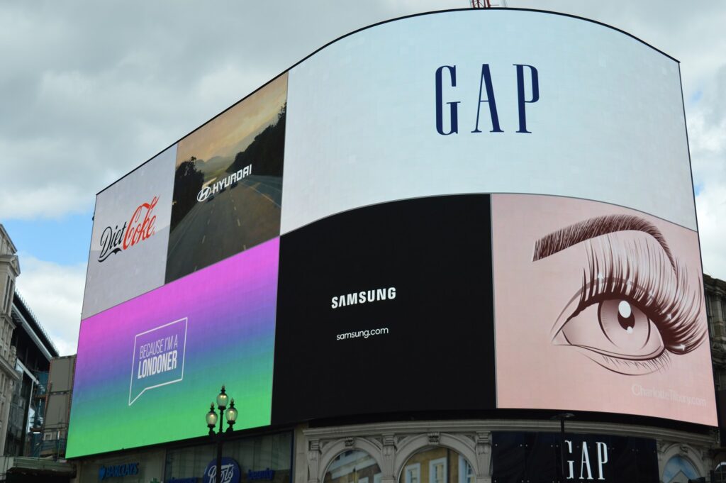 Large curved outdoor LED advertising screen in a busy city location, displaying multiple brand adverts.