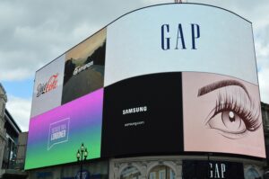Large curved outdoor LED advertising screen in a busy city location, displaying multiple brand adverts.