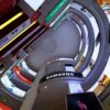 Aerial view of digital advertising screens and branded storefronts along a curved multi-storey shopping mall atrium.