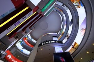 Aerial view of digital advertising screens and branded storefronts along a curved multi-storey shopping mall atrium.
