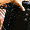 Musician adjusting the control panel of a Bose S1 Pro+ Wireless PA System, with a guitar positioned alongside for a live performance setup.