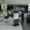 Black 55-inch touchscreen freestanding digital poster in a car showroom, displaying vehicle model information.