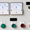 Industrial control panel showing voltage and current meters alongside start, stop, and overload push buttons.