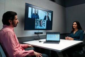 Bose Videobar mounted beneath a display in a meeting room, in use during a video conference call.