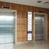 76-inch ultra-wide stretched bar display mounted vertically between two lifts, showing a floor-by-floor office directory.
