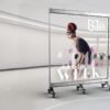 Freestanding transparent LED screen on castors, showing a fashion campaign image, with the retail space visible through the display.