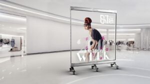 Freestanding transparent LED screen on castors, showing a fashion campaign image, with the retail space visible through the display.