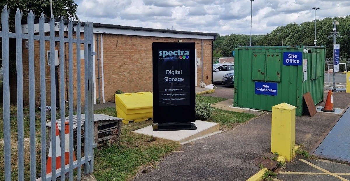 Outdoor digital signage totem installed at a recycling centre entrance, positioned near the site office and weighbridge.