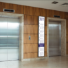 Ultra-wide stretched digital display showing floor directory information, mounted between two lift doors.