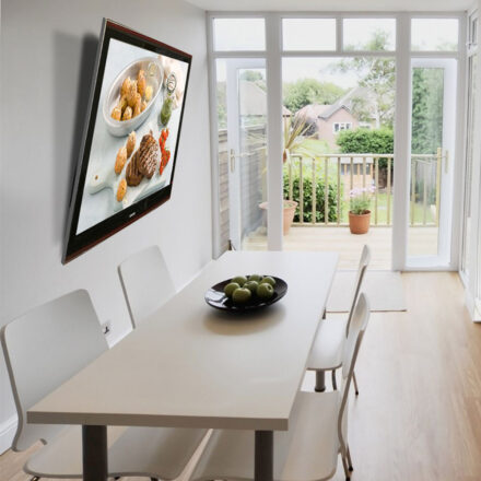 LC0946T tilting wall mounting bracket installed in a home dining room, holding a screen angled downward above a dining table showing a food advertisement.